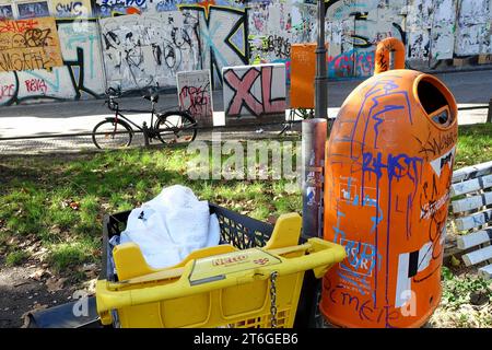 Mülleimer, Graffiti, Schriftzug XL und bunte Hausfassade - DE, Deutschland, Berlin, 16.10.2023 - Berlin-Mitte Ortsteil Wedding: Müll in einem abgestellten Einkaufswagen vor einem Abfallbehälter der BSR am Nettelbeckplatz. Im Bildhintergrund Fassade eines Gründerzeithauses mit Überresten von zuvor entfernten Plakaten, Graffiti und Schmierereien. Wilde Plakatierung wird, wenn der Verursacher erwischt wird, mit einer gebührenpflichtigen Beseitigungsanordnung geahndet Sachbeschädigung durch Plakatieren ist strafbar. Der S-Bahnhof Wedding ist in unmittelbarer Nähe. Der Platz wird häufig a Stockfoto