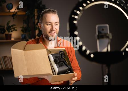 Ein Blogger mit Bart und Kamera zeigt eine vr-Brille und macht Videos in seinem Heimbüro. Rezension, Präsentationen, Auspacken für Blog zu Hause Stockfoto