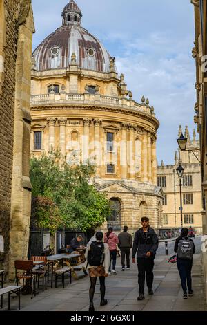 Leute, die in Catte Street, Oxford, England, Großbritannien, mit der Radcliffe Camera und Bodleian im Hintergrund unterwegs sind Stockfoto