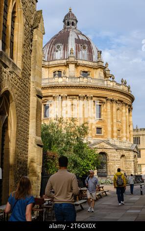 Leute, die in Catte Street, Oxford, England, Großbritannien, mit der Radcliffe Camera und Bodleian im Hintergrund unterwegs sind Stockfoto