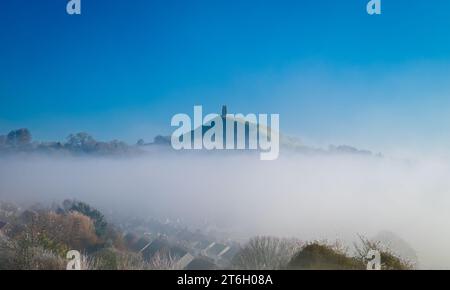 Ein Blick auf das Glastonbury Tor am frühen Wintermorgen vom Wearyall Hill mit Nebelbänken rund um das Tor und einem klaren blauen Himmel dahinter. Stockfoto