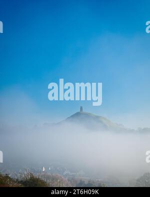 Ein Blick auf das Glastonbury Tor am frühen Wintermorgen vom Wearyall Hill mit Nebelbänken rund um das Tor und einem klaren blauen Himmel dahinter. Stockfoto