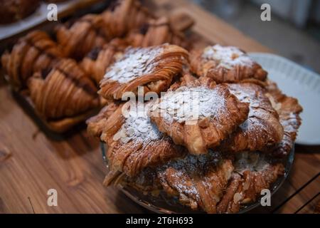 Hausgemachtes Croissant mit Mandelscheiben auf Glas und auf Holzhintergrund im Café, Bäckerei-Konzept Stockfoto