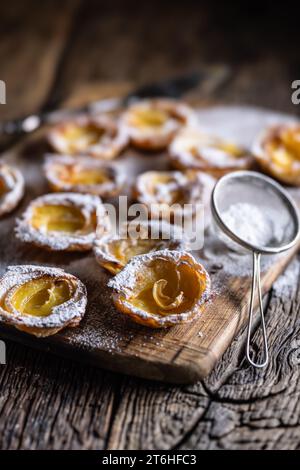 Mini-Torten aus Blätterteig und in Scheiben geschnittenen Äpfeln, bestreut mit Puderzucker auf hölzernem Schneidebrett. Frankreich Apfelkuchen - Nahaufnahme. Stockfoto