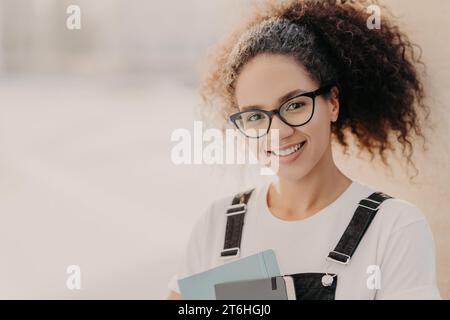 Lächelnder Akademiker mit Brille und lockigem Haar, mit einem Tablet in einem stilvollen Pullover. Stockfoto