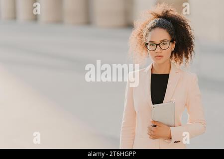 Professionelle Frau in einem schicken Anzug mit einem Tablet im Freien, mit einem selbstbewussten Look Stockfoto