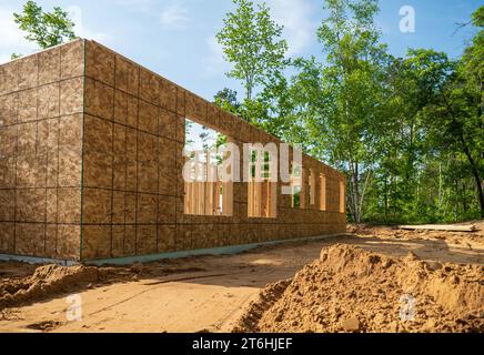 Neue Baustelle im frühen Baustadium, mit Sperrholz an den Außenwänden und Holzrahmenstollen innen, auf einem bewaldeten Grundstück. Stockfoto