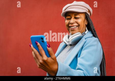 Ältere afrikanische Frau, die Spaß mit ihrem mobilen Smartphone im Freien hat Stockfoto