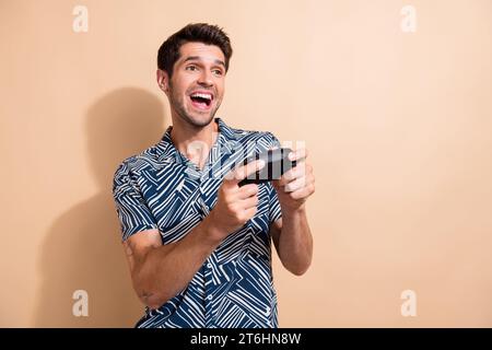 Foto eines verrückten jungen Mannes, der Videospiele spielt und Joystick-süchtig hält, der Wochenendurlaub auf beigefarbenem Hintergrund genießt Stockfoto