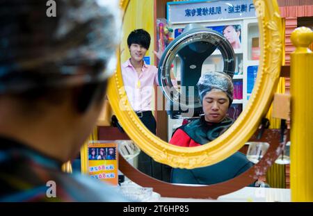 China, Shanghai, Friseur in Sichuan Lu, junger Mann unter Trockenhaube, sein Friseur schaut zu Stockfoto