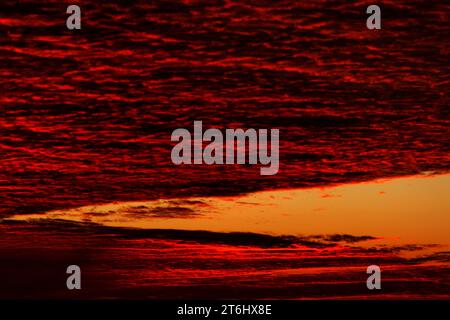 Wunderschöner farbenfroher, dramatischer Himmel mit Wolken bei Sonnenuntergang oder Sonnenaufgang. Heller farbenfroher Sonnenuntergang über Silhouetten von Wohngebäuden im Cottage Village. Stockfoto