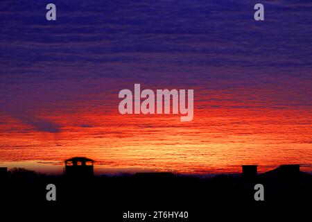 Wunderschöner farbenfroher, dramatischer Himmel mit Wolken bei Sonnenuntergang oder Sonnenaufgang. Heller farbenfroher Sonnenuntergang über Silhouetten von Wohngebäuden im Cottage Village. Stockfoto