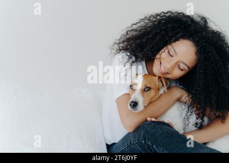 Eine ruhige Frau mit lockigen Haaren, die ihren Hund liebevoll umschließt und einen friedlichen Moment teilt Stockfoto