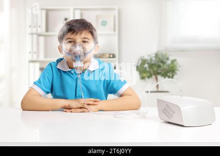 Junge, der an einem Tisch sitzt und einen Vernebler mit Nebel auf weißem Hintergrund benutzt Stockfoto