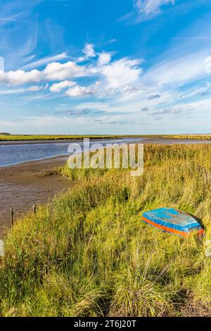 Bei Ebbe ist das Wattenmeer an der Mündung des Jade River in die Jade Bay sichtbar. Im angrenzenden Schilf ist ein blau-rotes Ruderboot aufgedreht. Stockfoto