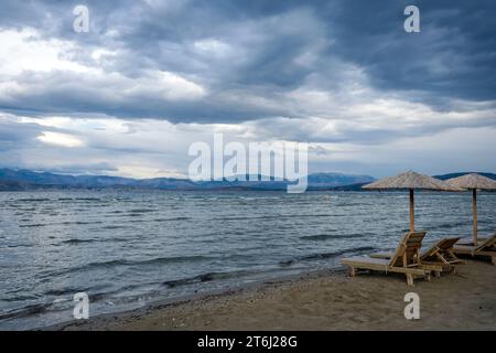 Kalamaki, Korfu, Griechenland, Sonnenliegen und Sonnenschirme am Kalamaki Strand im Nordosten der griechischen Insel Korfu, im Hintergrund das Festland Albaniens mit dem Badeort Saranda. Stockfoto