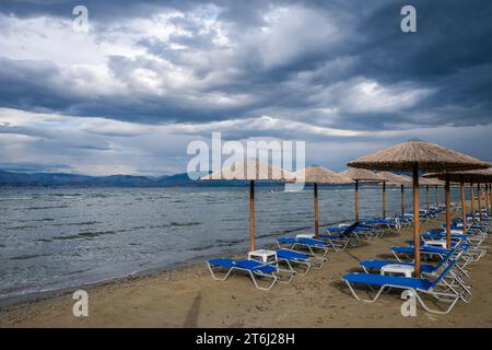 Kalamaki, Korfu, Griechenland, Sonnenliegen und Sonnenschirme am Kalamaki Strand im Nordosten der griechischen Insel Korfu, im Hintergrund das Festland Albaniens mit dem Badeort Saranda. Stockfoto