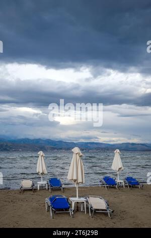 Kalamaki, Korfu, Griechenland, Sonnenliegen und Sonnenschirme am Kalamaki Strand im Nordosten der griechischen Insel Korfu, im Hintergrund das Festland Albaniens mit dem Badeort Saranda. Stockfoto