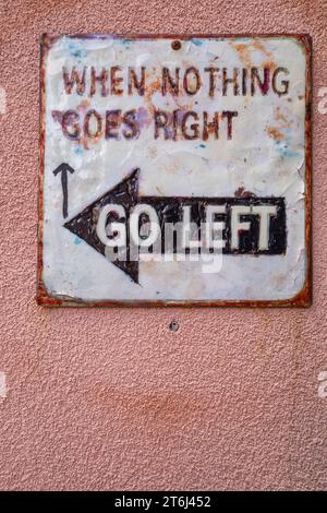 Vintage-Richtungstafel hängt an einer pinkfarbenen Wand mit lustigem Schriftzug „When Nothing Goes Right Go Left“ Stockfoto