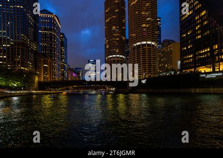 Spazieren Sie nachts entlang des Chicago Riverwalk. Blick auf Marina City, zwei runde Wolkenkratzer aus dem Jahr 1964, auch bekannt als Maiskolben. Marina Tower bei Nacht. Zwei 179,2 Meter hohe Doppeltürme gehören zu den berühmtesten Gebäuden Chicagos. Sie werden aufgrund ihres äußeren Erscheinungsbildes als „Maiskolben“ bezeichnet. Die unteren 19 Etagen bieten Platz für 896 Autos. Chicago, Illinois, Usa Stockfoto