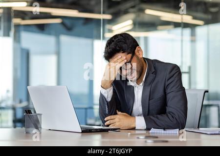 Depression am Arbeitsplatz, Geschäftsmann enttäuscht von den Ergebnissen der Leistung traurig in der Verzweiflung im Büro, Mann im Business-Anzug unglücklich mit Laptop zu arbeiten. Stockfoto