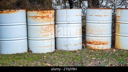 Eine Nahaufnahme von fünf weißen, rostigen Metallfässern hintereinander gegen eine unscharfe Baumlinie in Missouri. Stockfoto