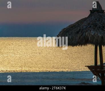 Die Gewässer des Golfs von Mexiko tanzen bei Sonnenuntergang an diesem Strand in Florida, während Himmel und Wasser in die Nacht verschwinden und nur die silloettierten Strohdächer von hinterlassen Stockfoto