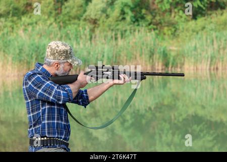 Mann, der mit Jagdgewehr in der Nähe des Sees im Freien zielt Stockfoto