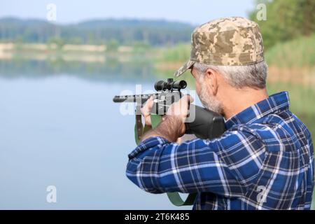 Mann mit Jagdgewehr in der Nähe des Sees im Freien. Leerzeichen für Text Stockfoto