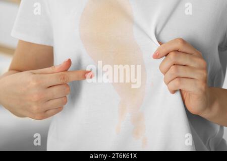 Frau zeigt Flecken von Kaffee auf ihrem Hemd drinnen, Nahaufnahme Stockfoto