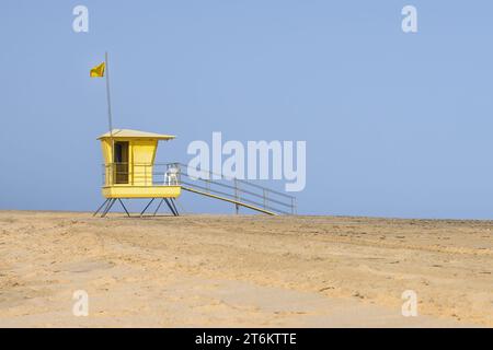 Gelber Rettungsschwimmerturm am Strand mit gelber Strandsicherheitsfahne vor blauem Himmel. Kopierbereich. Stockfoto