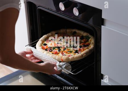 Frau stellt die Pizzapfanne aus der Nähe in den Ofen Stockfoto