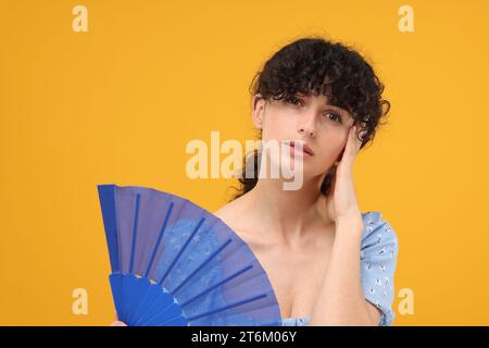 Frau mit Handventilator, die an Hitze auf orangem Hintergrund leidet Stockfoto