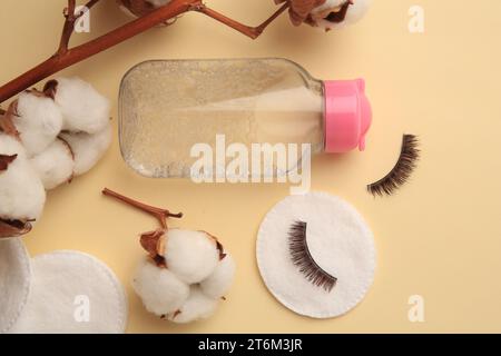 Flasche Make-up-Entferner, Baumwollblumen, Pads und falsche Wimpern auf gelbem Hintergrund, flach gelegt Stockfoto