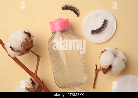 Flasche Make-up-Entferner, Baumwollblumen, Pads und falsche Wimpern auf gelbem Hintergrund, flach gelegt Stockfoto