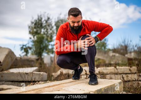 Der junge Mann hat Schmerzen im Knie, während er im Freien trainiert. Stockfoto