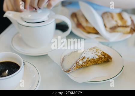 Süße Cannoli gefüllt mit Sahne und einer Tasse schwarzen Kaffee zum Frühstück auf einem Tisch in einem Café. Italienisches Gebäck. Stockfoto