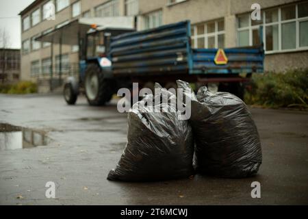 Zwei Müllsäcke auf dem Hintergrund des Traktors. Garbage Collection vor Ort. Müllsäcke auf der Straße. Gartenreinigung. Stockfoto