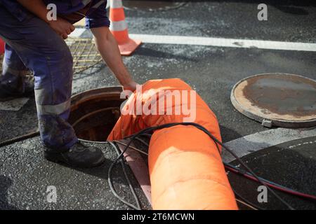 Reparatur der Kanalisation. Fördern von Abfällen aus der Luke. Öffnen Sie die Klappe. Der Arbeiter steuert die Luftzufuhr. Abwasserunfall. Stockfoto