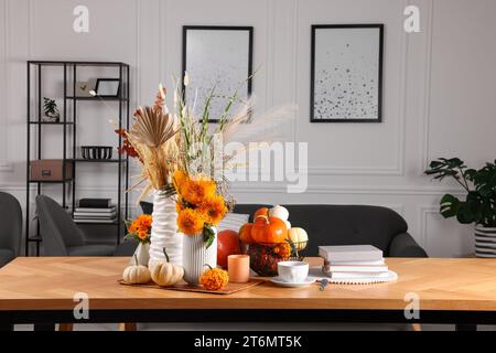 Wunderschöne Herbstkomposition mit leuchtend orangen Blumen und Kürbissen auf Holztisch im Zimmer Stockfoto