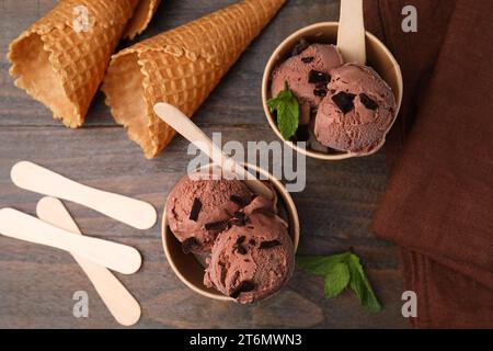 Pappbecher mit leckerem Schokoladeneis, Sticks, Minzblättern und -Zapfen auf Holztisch, flach gelegt Stockfoto