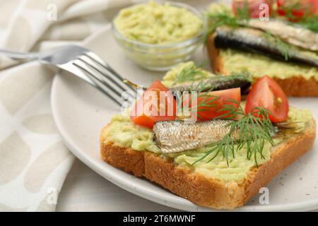 Köstliche Sandwiches mit Sprats, Tomaten, Dill und Avocadopüree auf weißem Tisch serviert, Nahaufnahme Stockfoto