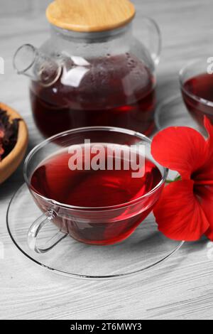 Köstlicher Hibiskus-Tee und wunderschöne Blume auf hellem Holztisch Stockfoto