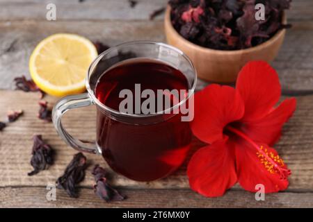 Köstlicher Hibiskus-Tee und schöne Blume auf Holztisch, Nahaufnahme Stockfoto