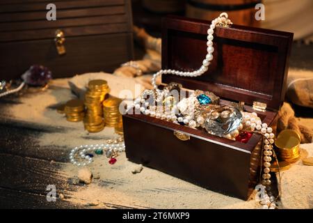 Truhe mit Schätzen und verstreutem Sand auf Holztisch Stockfoto