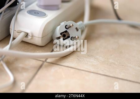 Überlastete Stromversorgungsplatinen. Steckdosenleisten mit verschiedenen Steckern auf weißem Boden. Konzept der Gefahr Gefahr Überlaststrom elektrisch Stockfoto