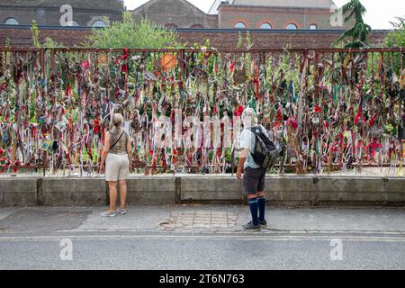 Zwei Personen halten an und schauen sich die Bänder und Nachrichten vor dem Friedhof Crossbones und dem Erinnerungsgarten in London an Stockfoto