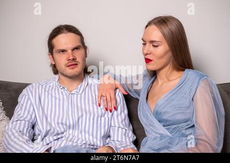 Ernsthaftes Paar in hellblauer Kleidung sitzt auf einem Sofa und umarmt sich. Kopierbereich. Hintergrund für Zitate. Hochwertige Fotos Stockfoto