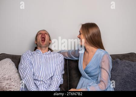 Ein verschlafener Mann in einem gestreiften Hemd gähnt und eine ironische Frau mit langen Haaren, knallroten Nägeln, in einem blassblauen Kleid. Kopierbereich. Hintergrund für Zitate. H Stockfoto