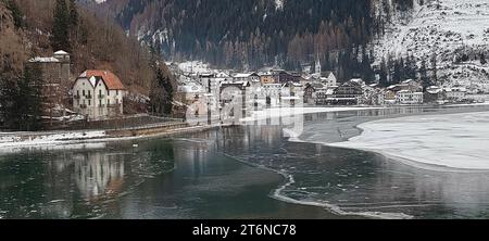 Blick auf Häuser und verschneite Stadt Alleghe vor dem teilweise gefrorenen See. Stockfoto